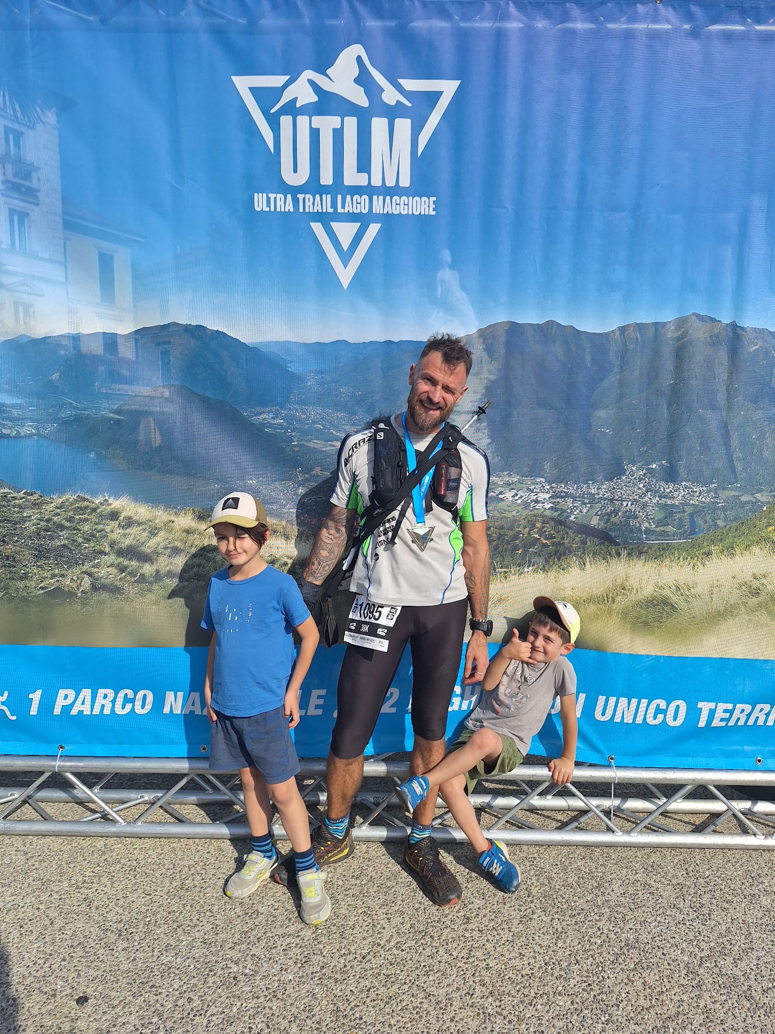 Tommi con la medaglia della BRAVE 38K davanti allo striscione UTLM insieme ai figli