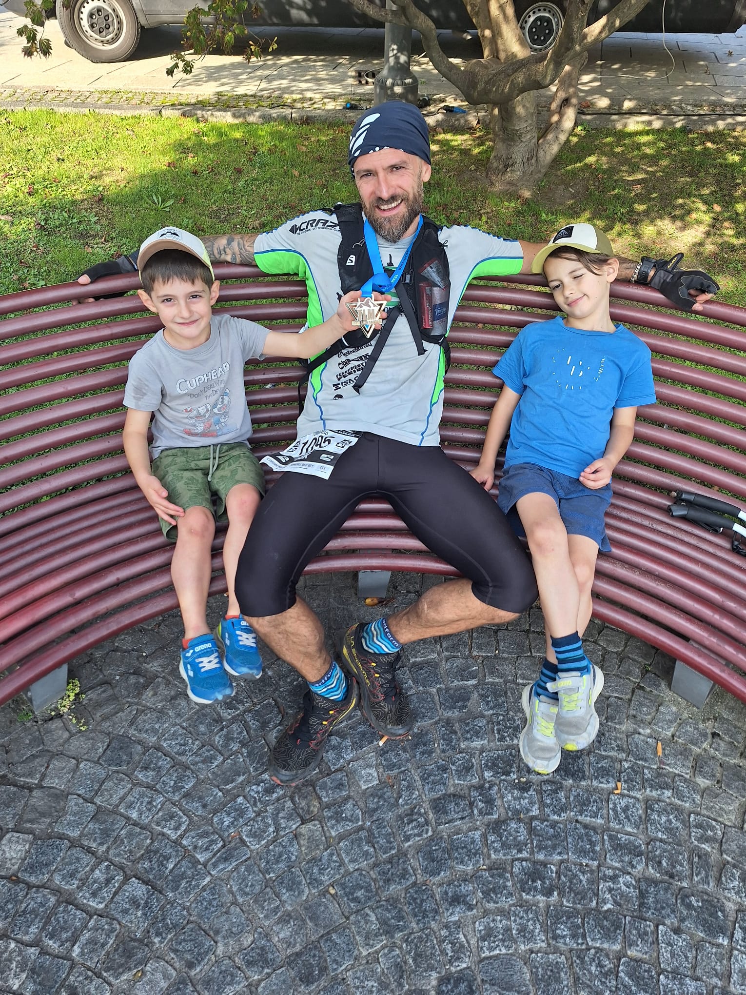Tommi con la medaglia della BRAVE 38K seduto su una panchina insieme ai figli dopo il Trail Lago Maggiore